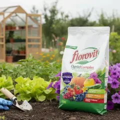 Torba nawozu Florovit OgrodComplex na tle grządki z warzywami, kwiatami i szklarnią.